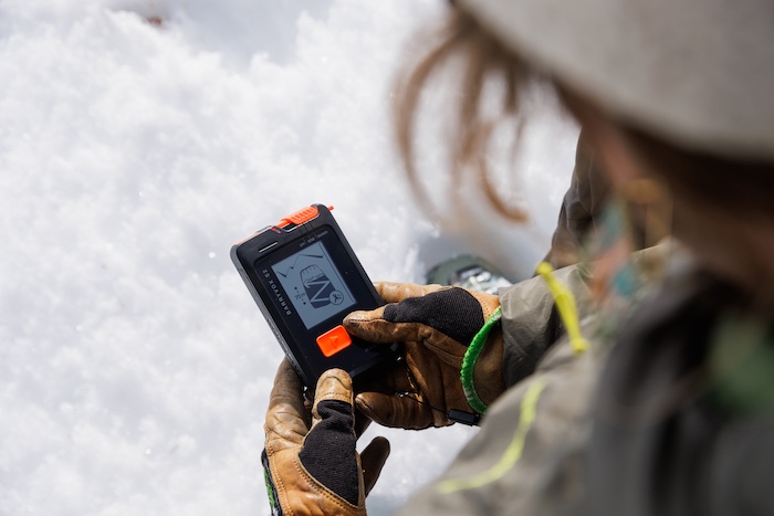 An avalanche forecaster practices using a beacon in the snow.