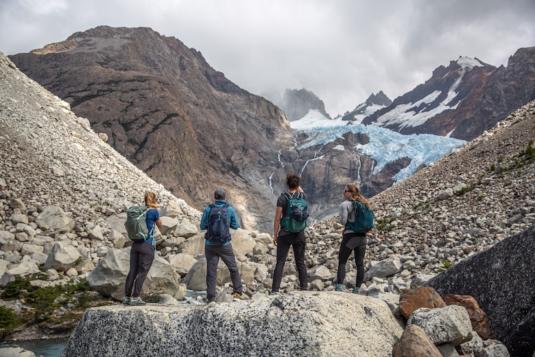 Four hikers standing on a large boulder looking off into mountains and a glacier