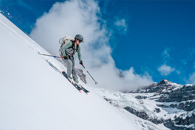 A skier rides down a snowy slope on a beautiful sunny day in the mountains.