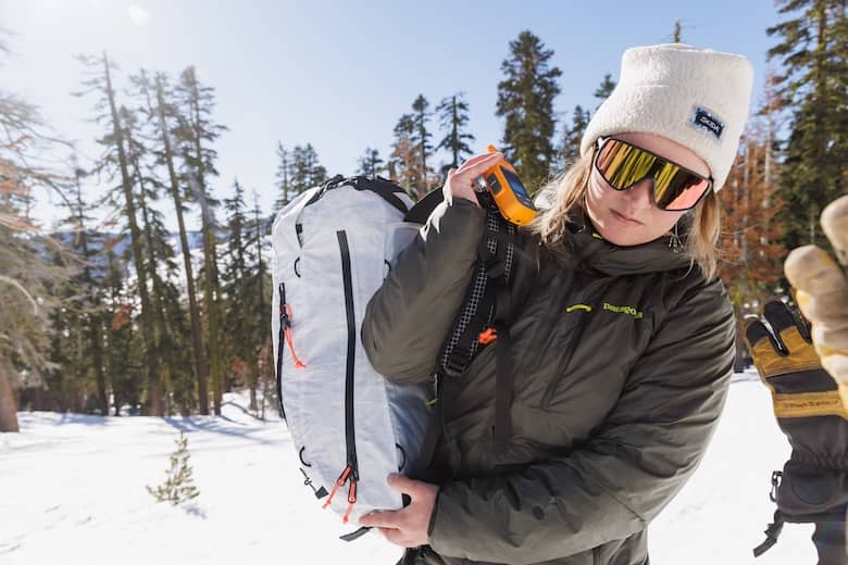 A woman wearing a Patagonia jacket pulls a backpack over her shoulder in the snowy mountains