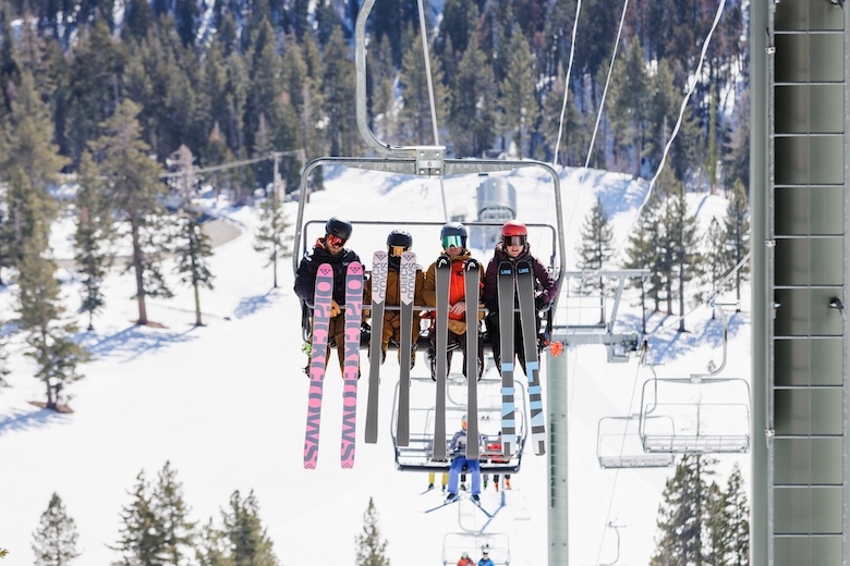 Skiiers show off their skis while riding up a ski lift.