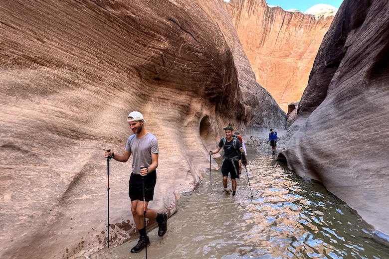 A group of hikers walk through a canyon filled with water
