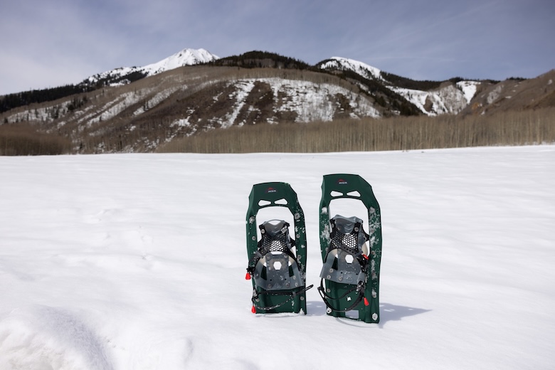 A pair of showshoes stick out of the snow with mountains in the background