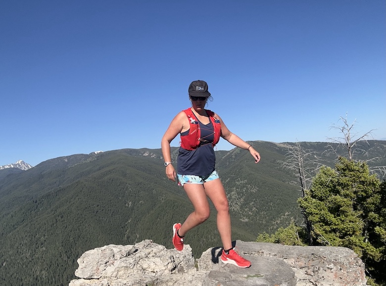 A runner on top of a peak in a red pair of the Salomon Pulsar shoe with a blue sky behind.