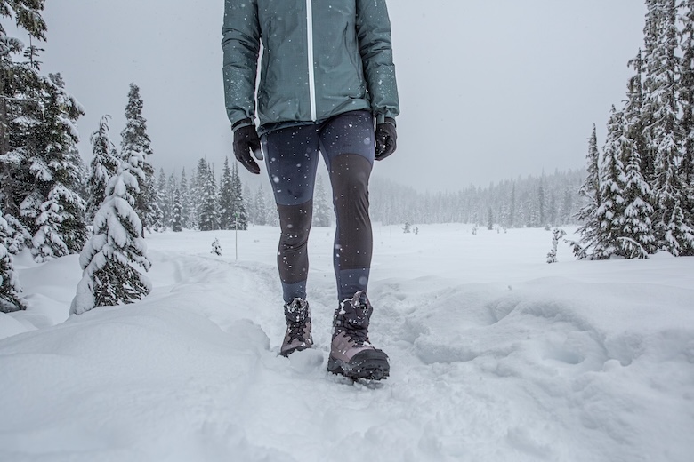 A woman walks along a snowy trail on a grey and stormy day