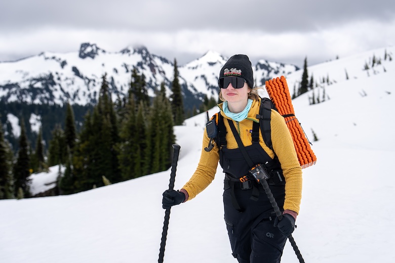 A smiling woman skins up on Mt. Rainier wearing ski bibs