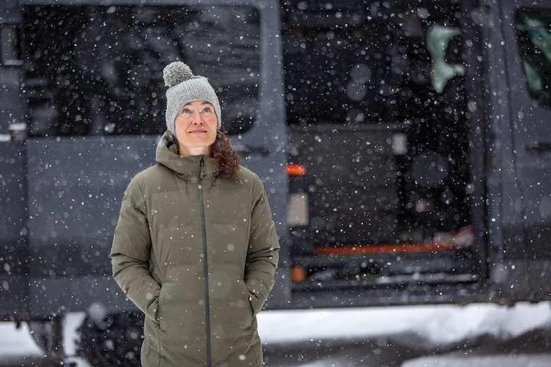 A woman walks in the snow and looks up at the sky