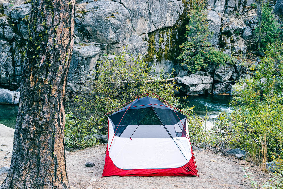 A heavy duty tent is perched on a campsite above an emerald green river.