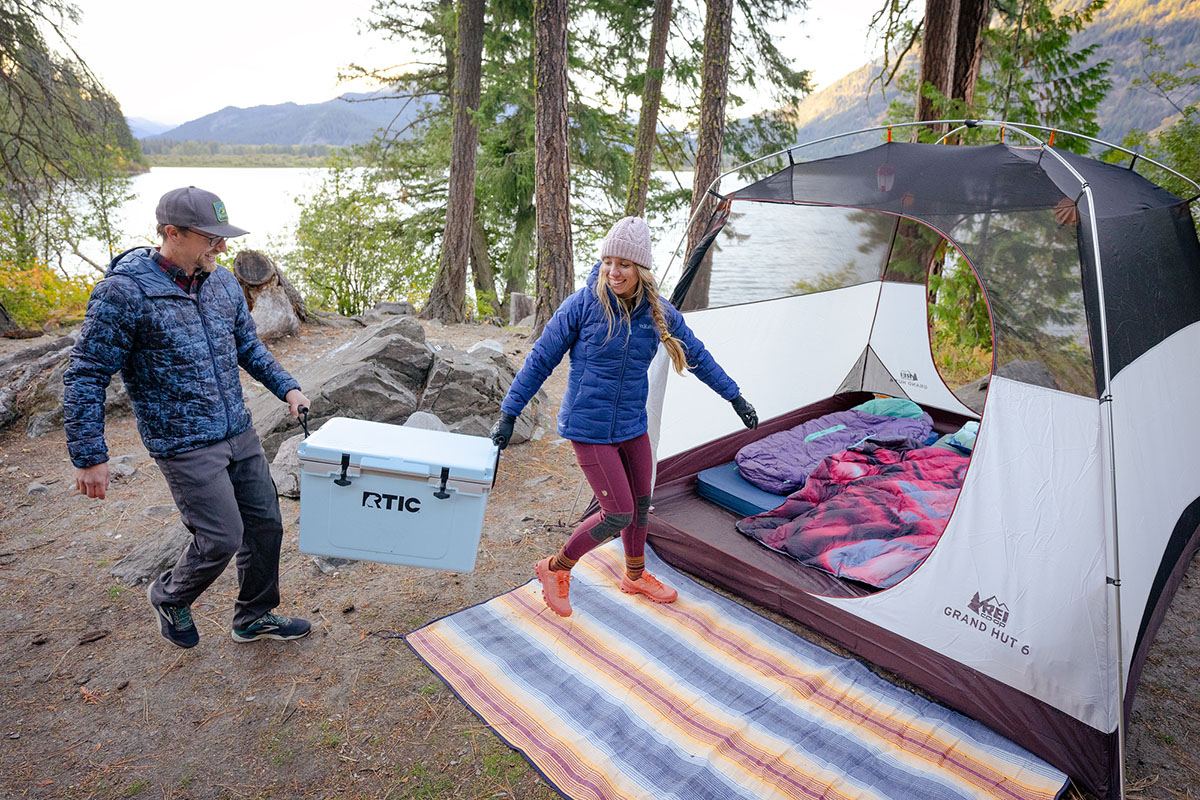 A couple sets up a cozy camp next to a lake, and opts to bring a cooler without wheels.