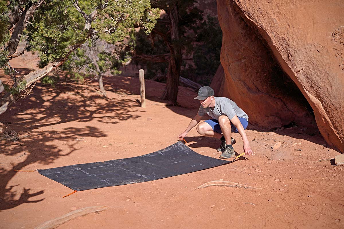 A man putting a budget backpacking tent foot print on the ground