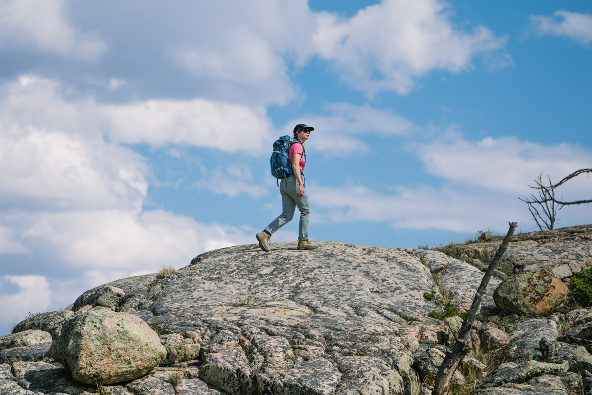 A hiker high up on a rocky ridge looks at the distant clouds.