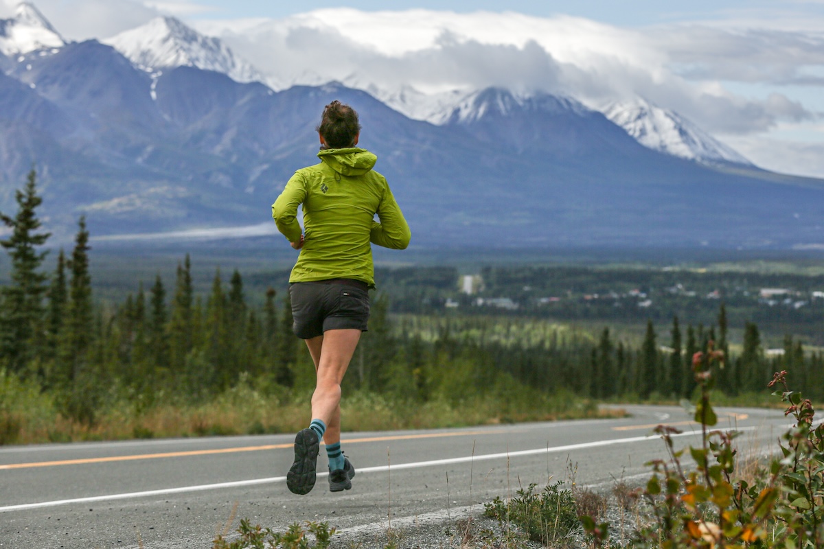 a woman runs away from the camera in front of a mountain range, testing shoes for review