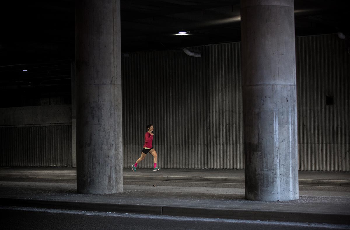 A female runner is running on pavement under a highway, moving fast