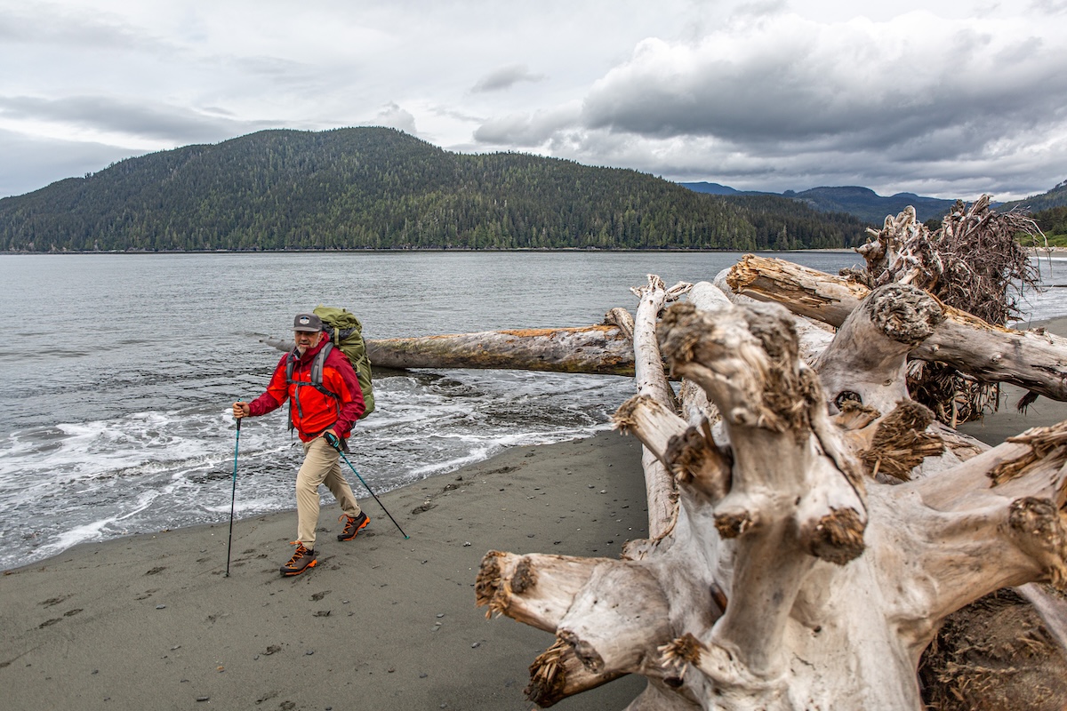 A man hikes on a beach while wearing a hardshell jacket