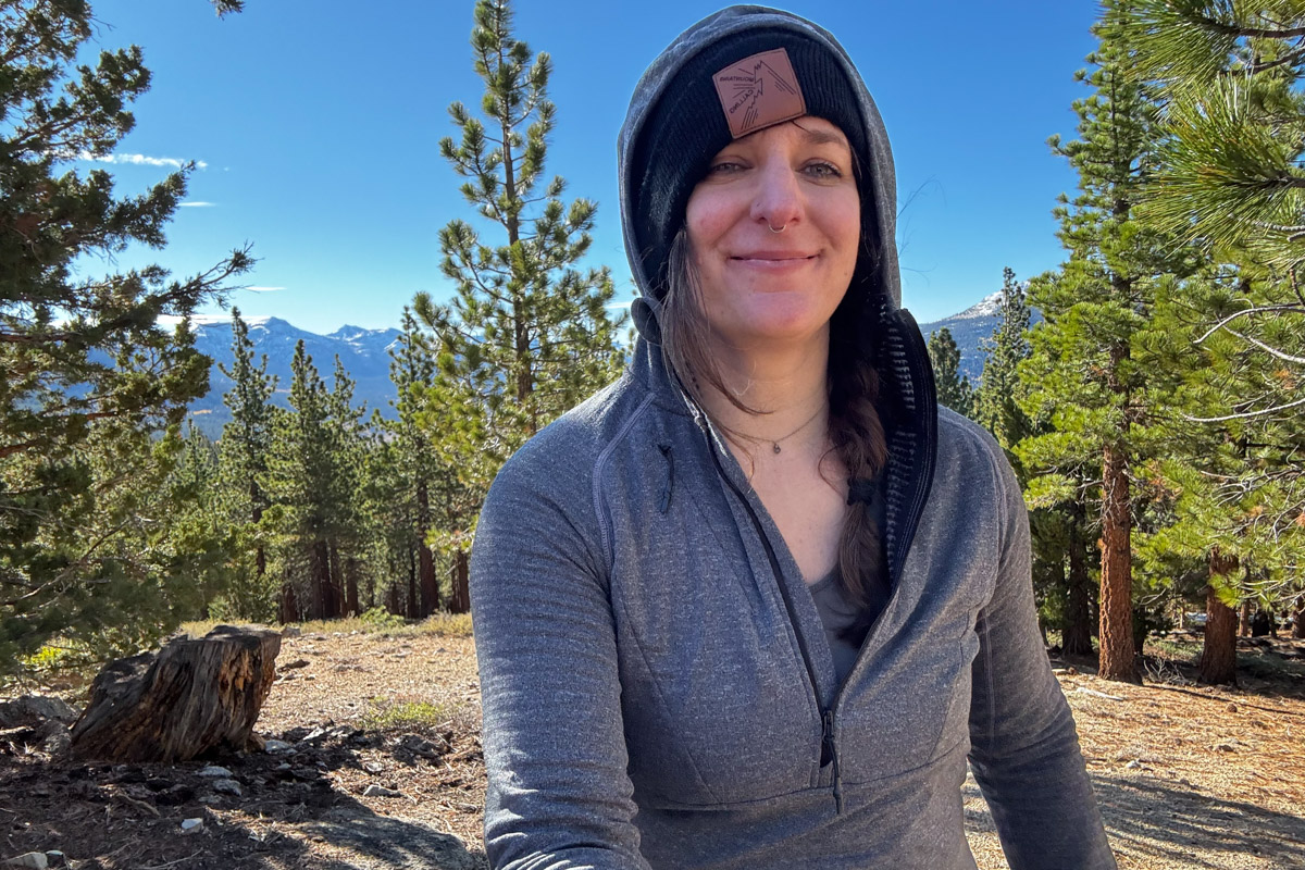 A woman smiling while wearing a grey baselayer in the woods.