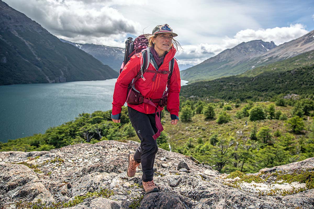 A woman treks over moss covered rocks in a beautiful mountain valley.