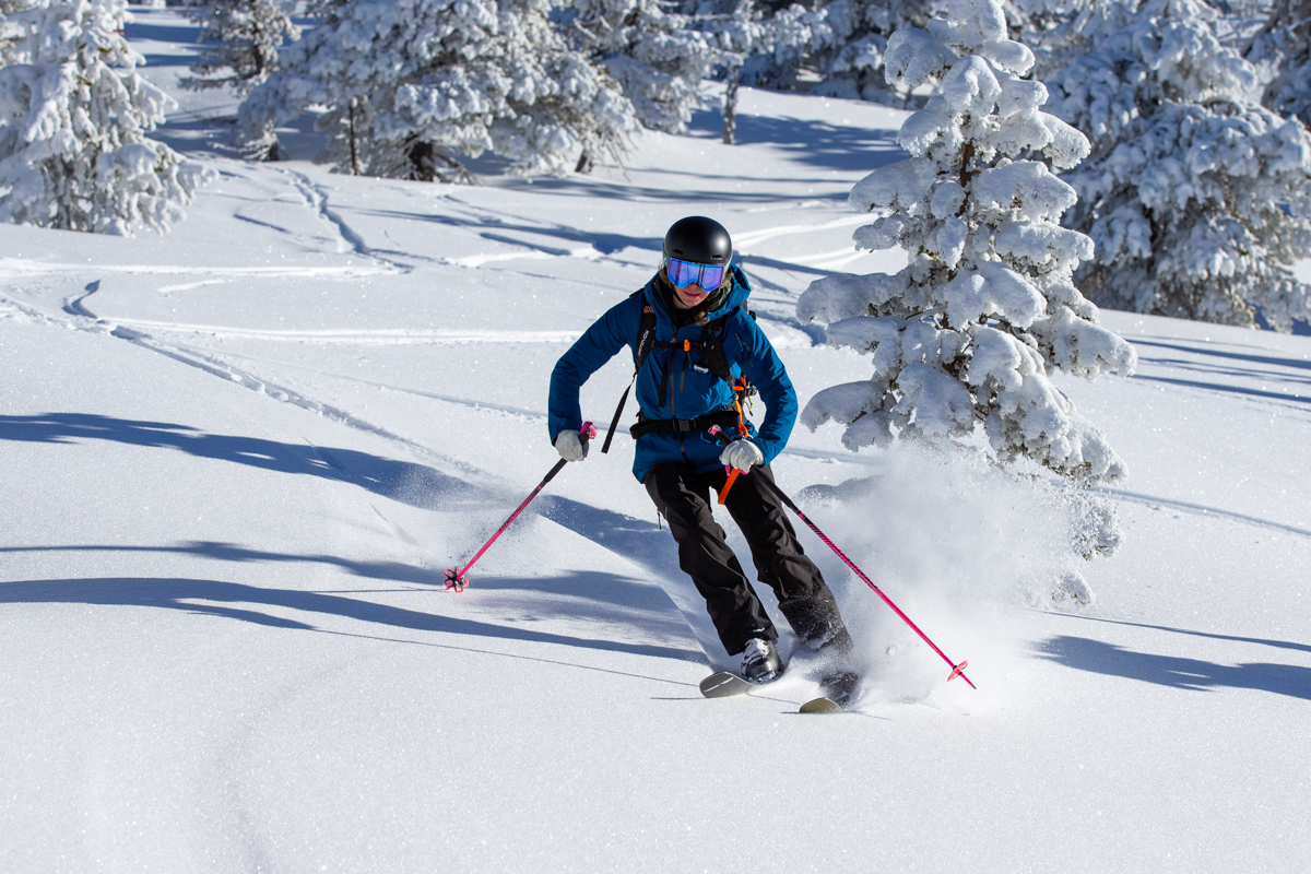 A woman skis down a snowy forest slope wearing black ski bibs