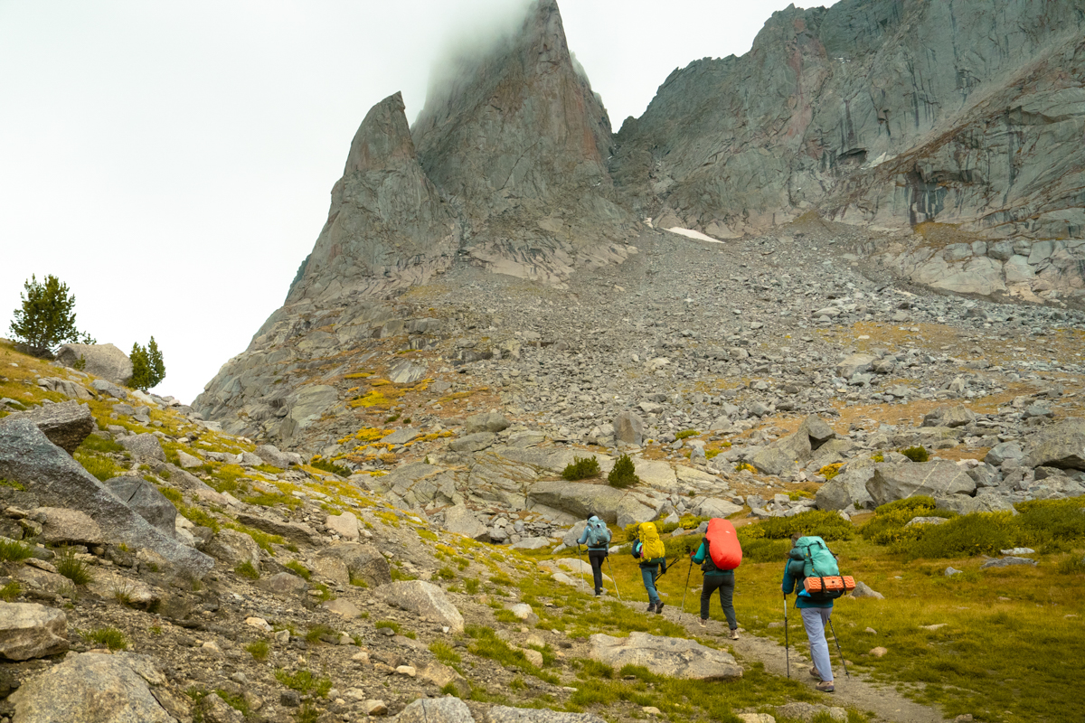 Four backpackers hike on trail through misty mountain backdrop