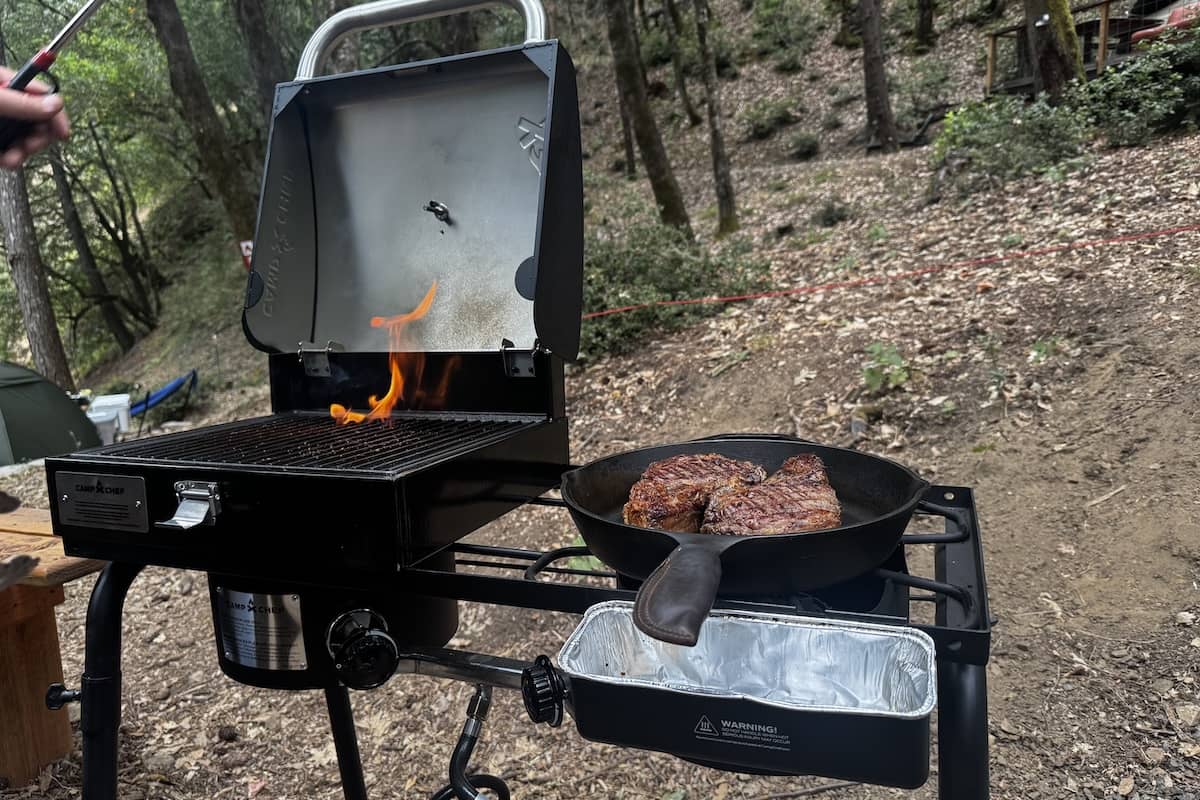 A freestanding stove with a grill box and a cast iron skillet with two large steaks cooking inside