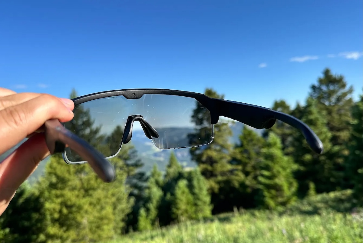 A hand holds up Chamelo music sunglasses against the blue sky