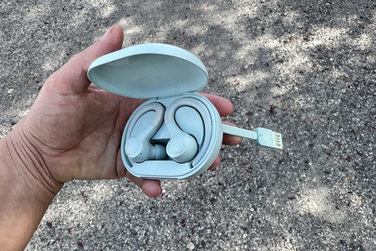 A hand holds a pair of headphones with the charging cable attached