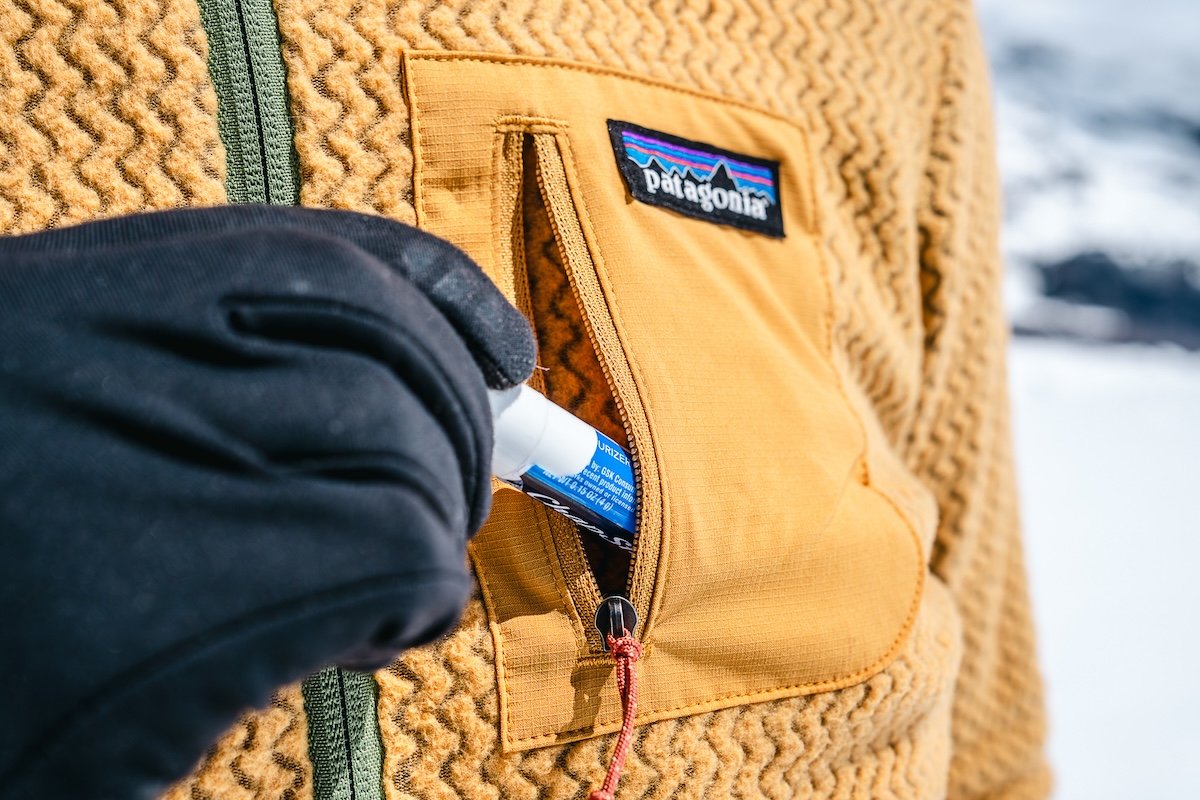 A close-up of putting chapstick in the chest pocket of the Patagonia R1 Hoody
