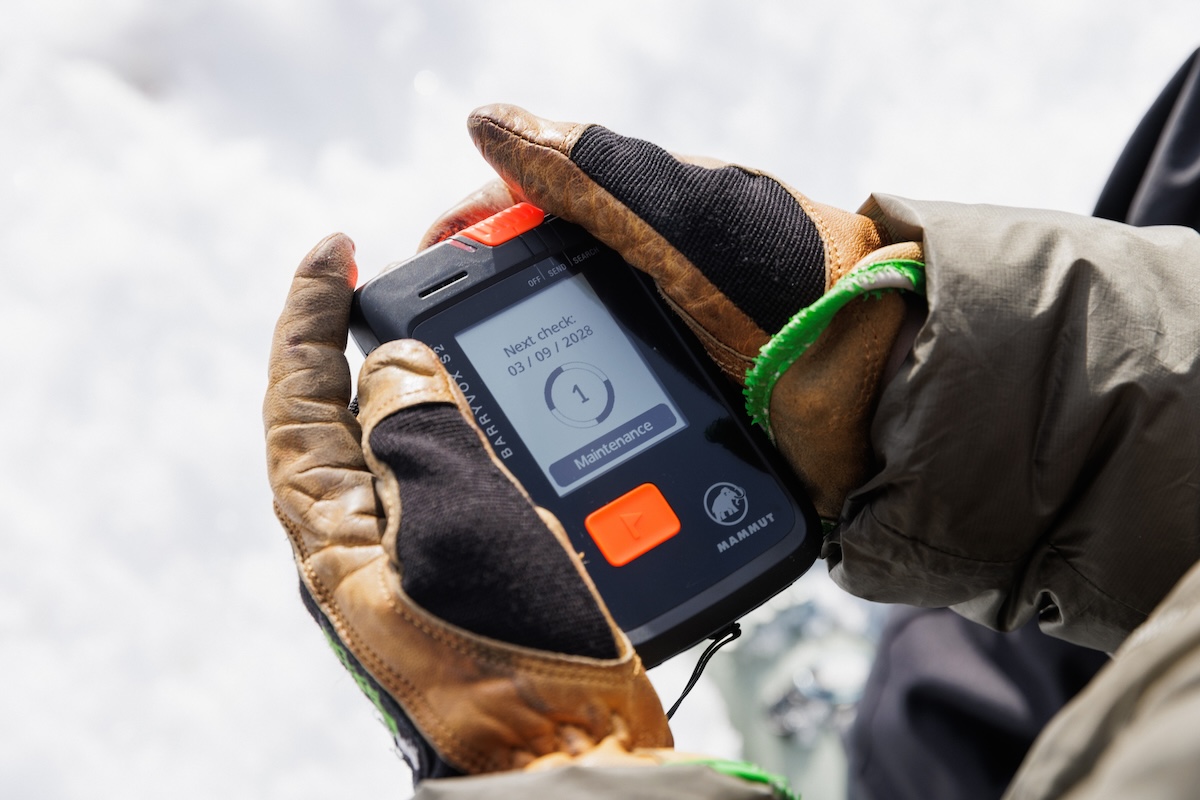 A close-up of gloved hands holding an avalanche beacon