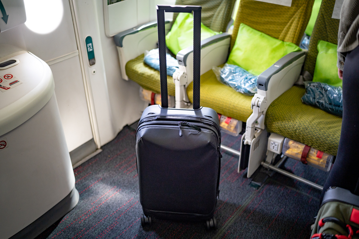 A slim, carbon suitcase waits next to a seat on a plane.