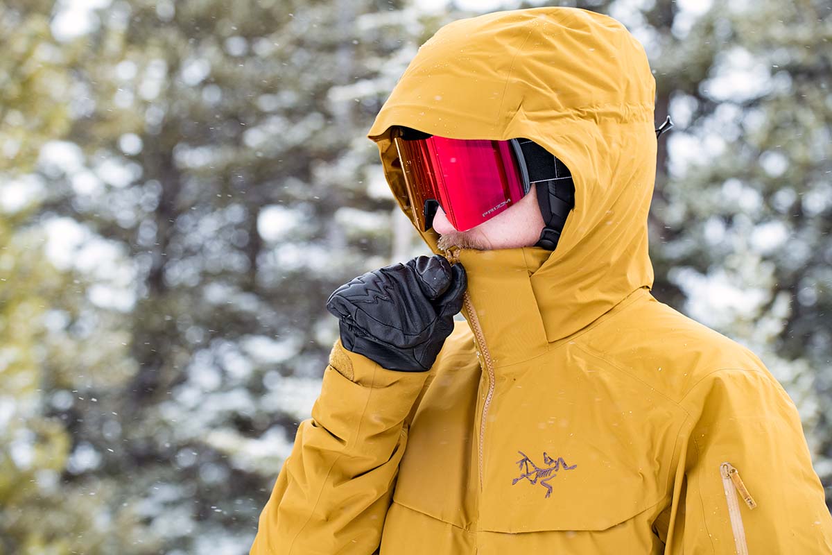 A skiier zips the collar up on his jacket hood, but it's short compared to other coats.