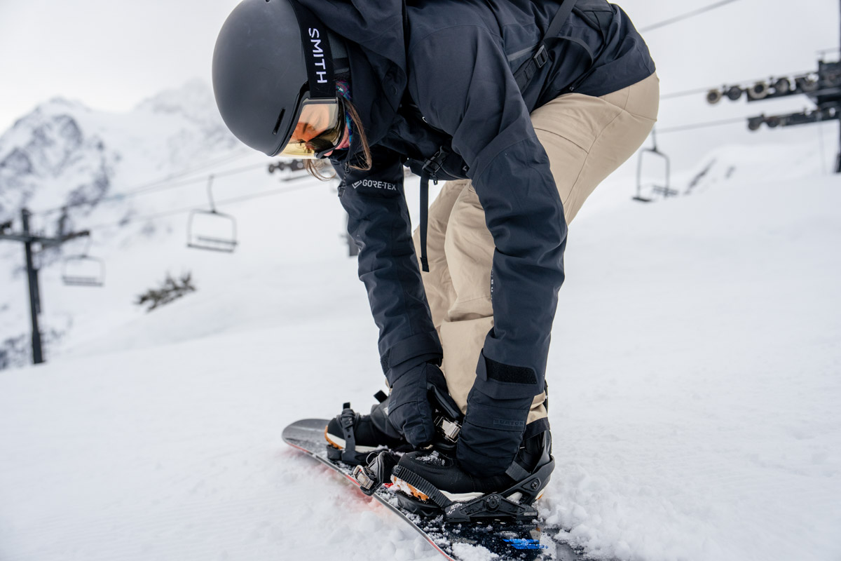 A woman bending over to adjust boots in snowboard pants