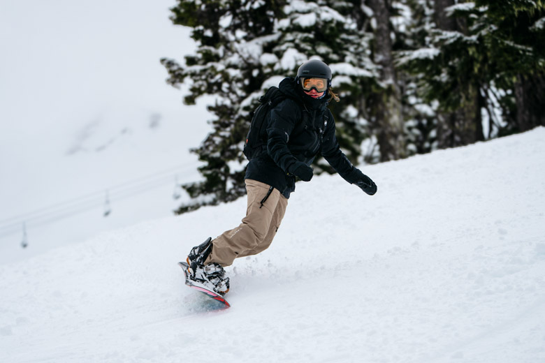A woman snowboarding down a slope in snowboard pants