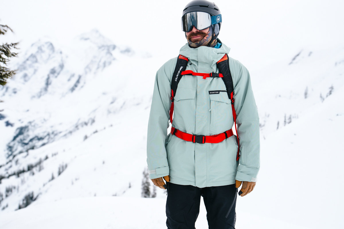 A man smiling in front of a winter landscape wearing a red ski backpack