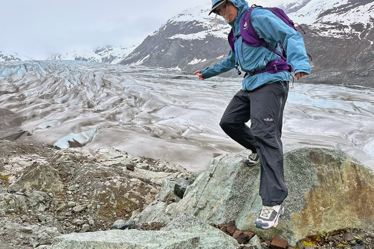 A woman stepping down a boulder while hiking in a purple daypack