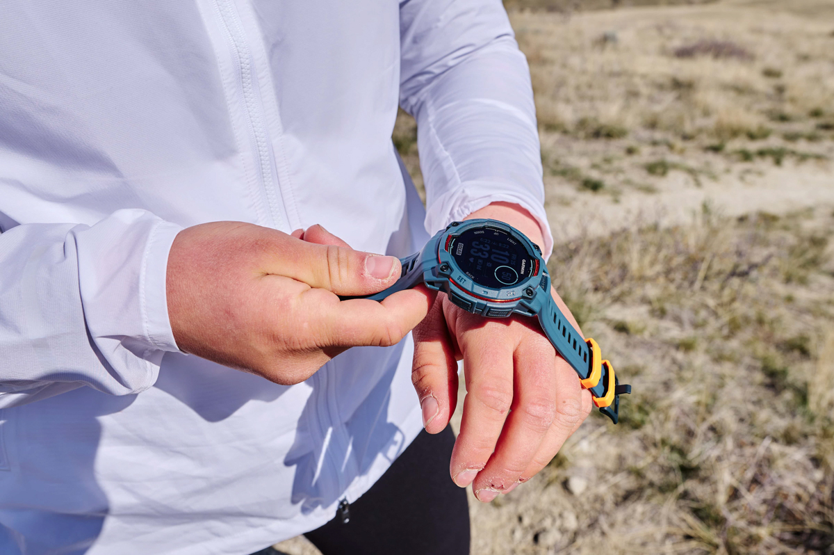 A close up of a hand putting a blue GPS watch on the other wrist