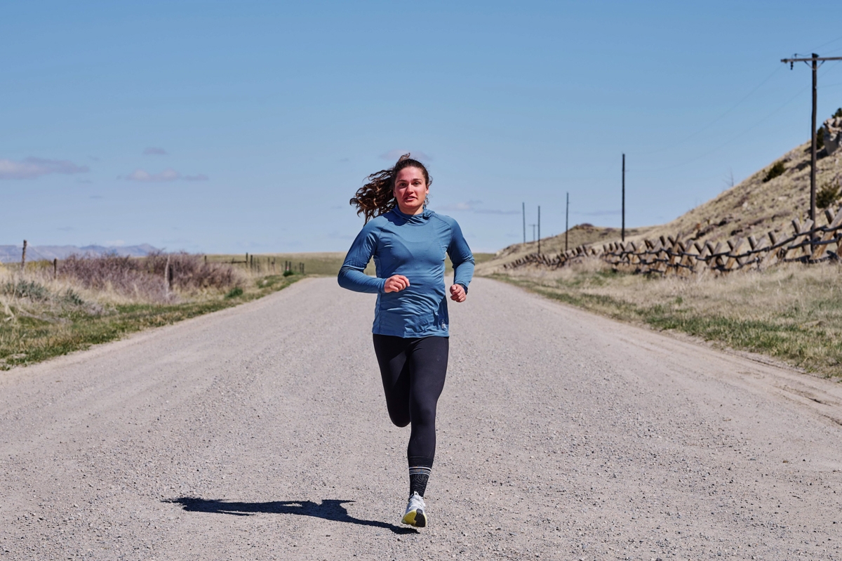 A woman running on a flat gravel road while wearing a blue GPS watch