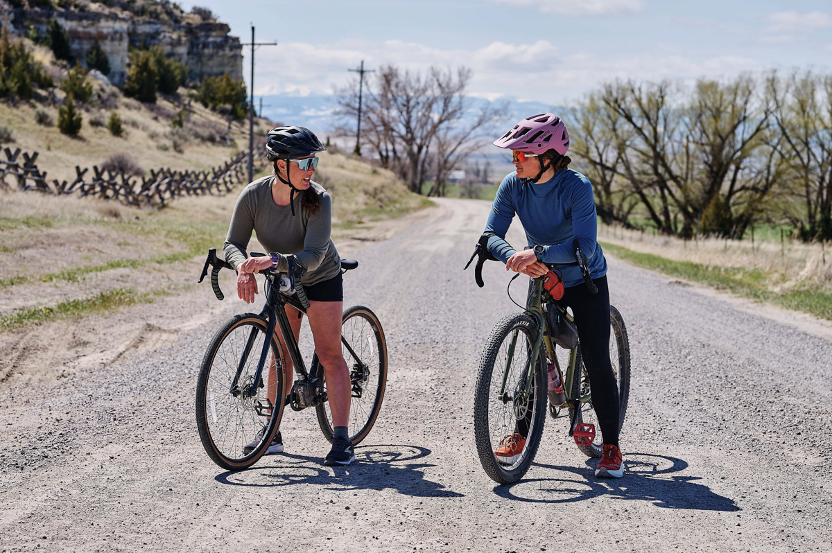 Two woman chat while sitting on bikes and one wears a blue GPS watch