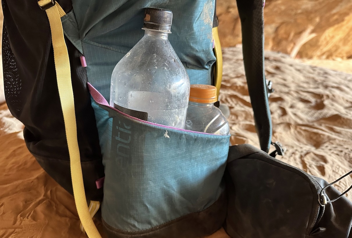 A close up image of the side pocket of the Mariposa backpack with two plastic water bottles in it