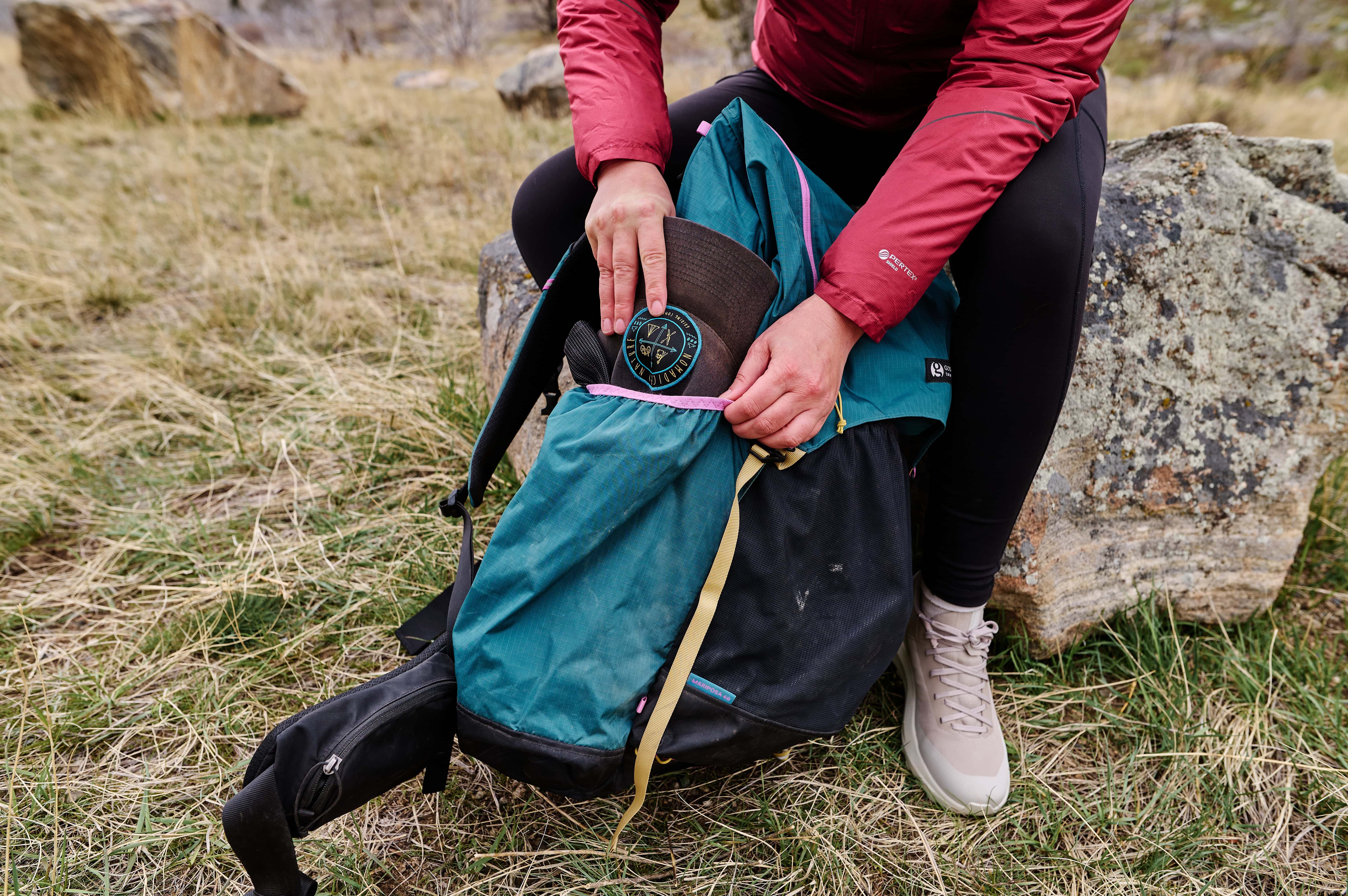 A backpacker tucks a hat into the side pocket of the Gossamer Gear Mariposa