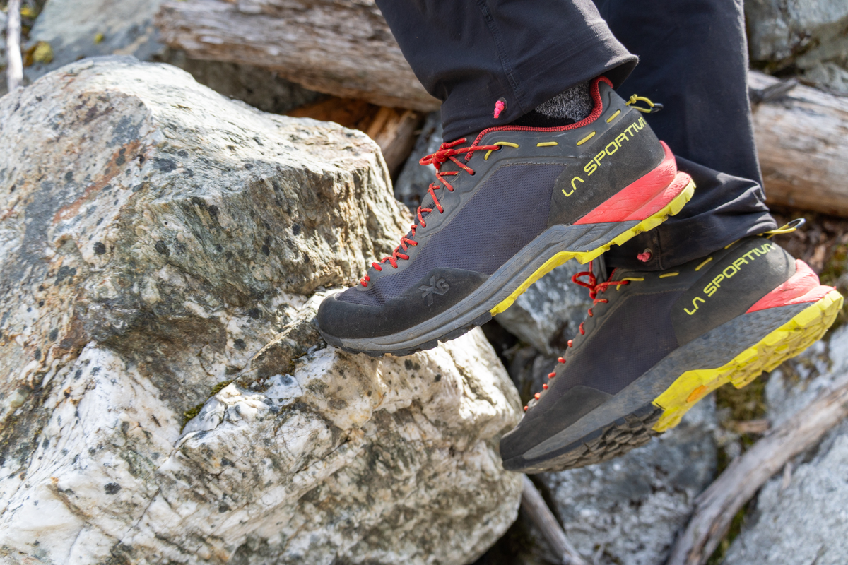 A close up of a grey and red approach shoe stepping on a small rock edge