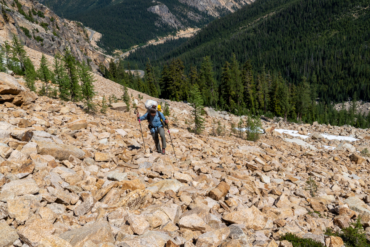 A man hiking up a steep rocky slope while wearing grey and red approach shoes