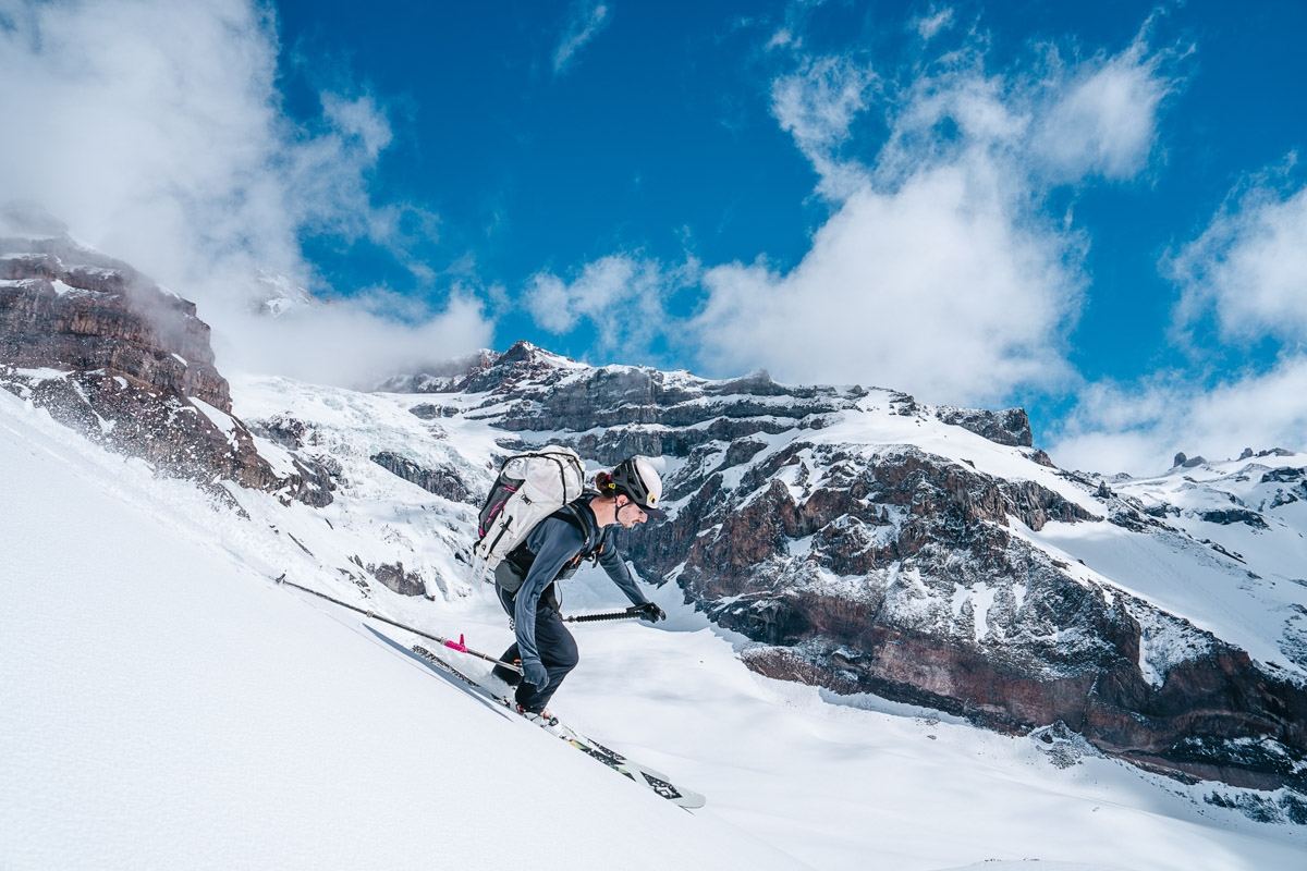 A man on skis with a backpacks skis down a snowy slope
