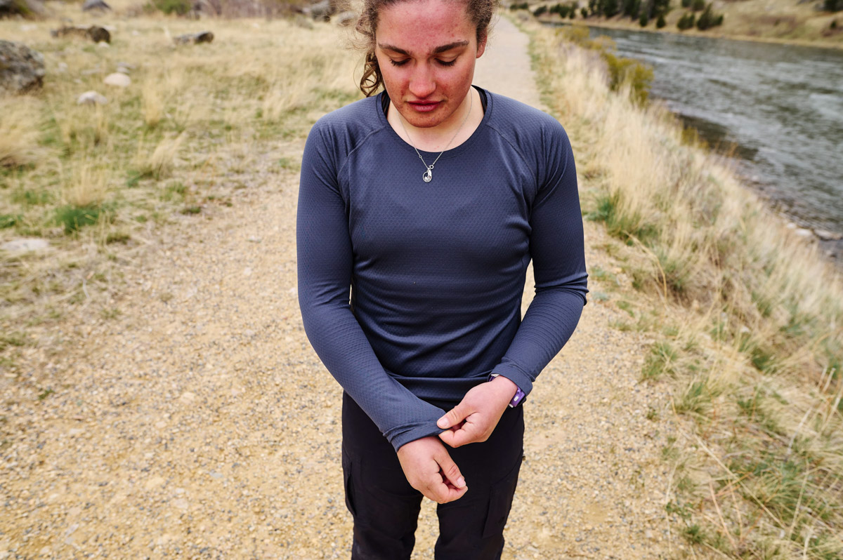 A woman on a trail next to a river adjusts the sleeve of the Patagonia Capilene Midweight shirt