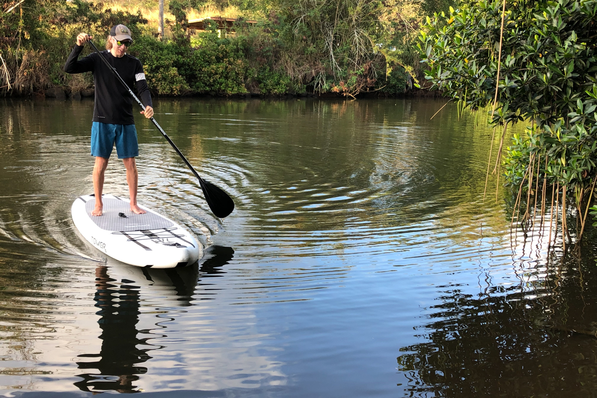A man paddling a black and white paddle board on still lake waters