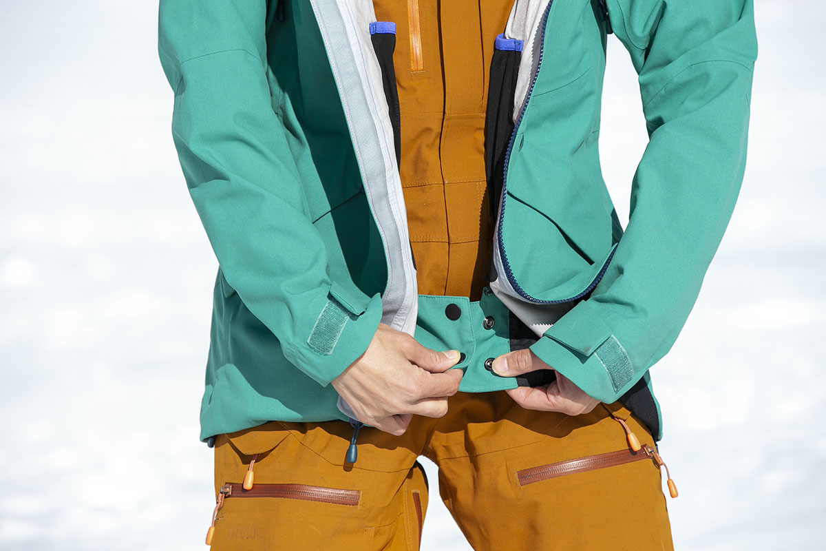 A closeup of a skier snapping the powder skirt together on a ski jacket