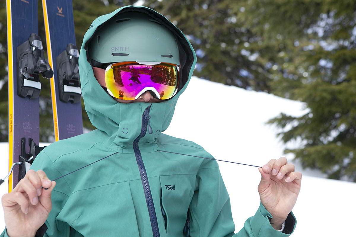 A close up of a skier with goggles and a helmet cinching down the Stella Primo jacket's hood