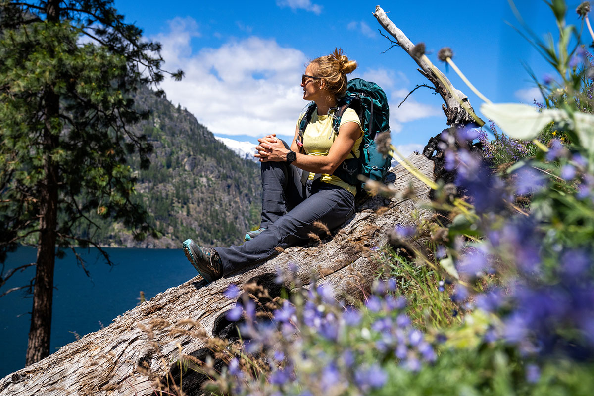 A woman sits on a rock in the sun with her backpack on. 