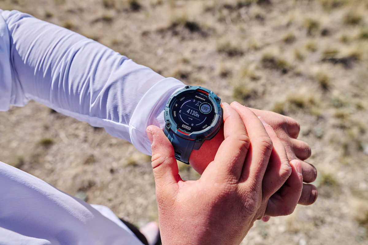 A close up of a blue GPS watch on a wrist while a hand toggles side buttons