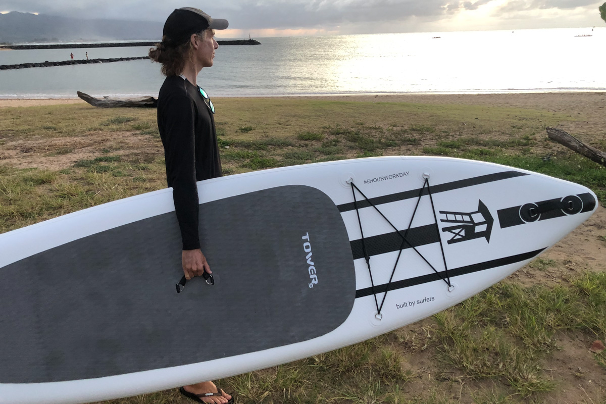 A man carrying a black and white paddle board to the beach at sunset