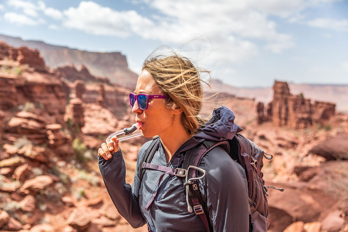 A woman drinks from a hydration backpack while hiking in the desert.