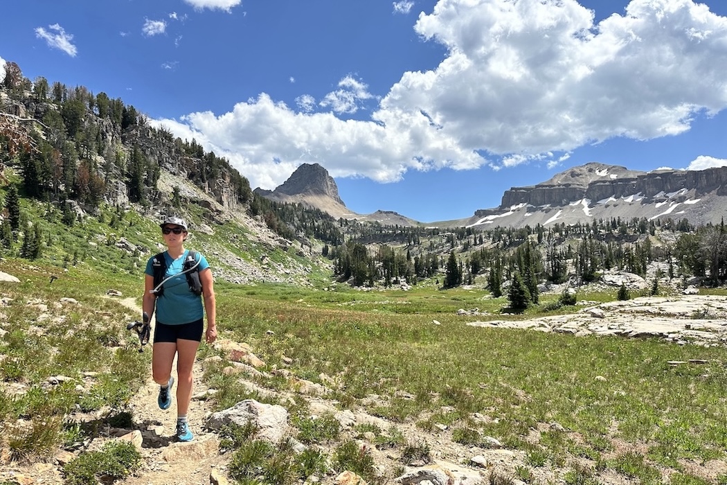 A woman hiking up a backpacking trail with mountain views behind her